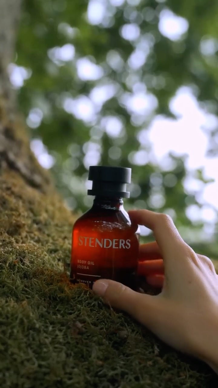 Hand holding STENDERS Jojoba body oil on mossy bark